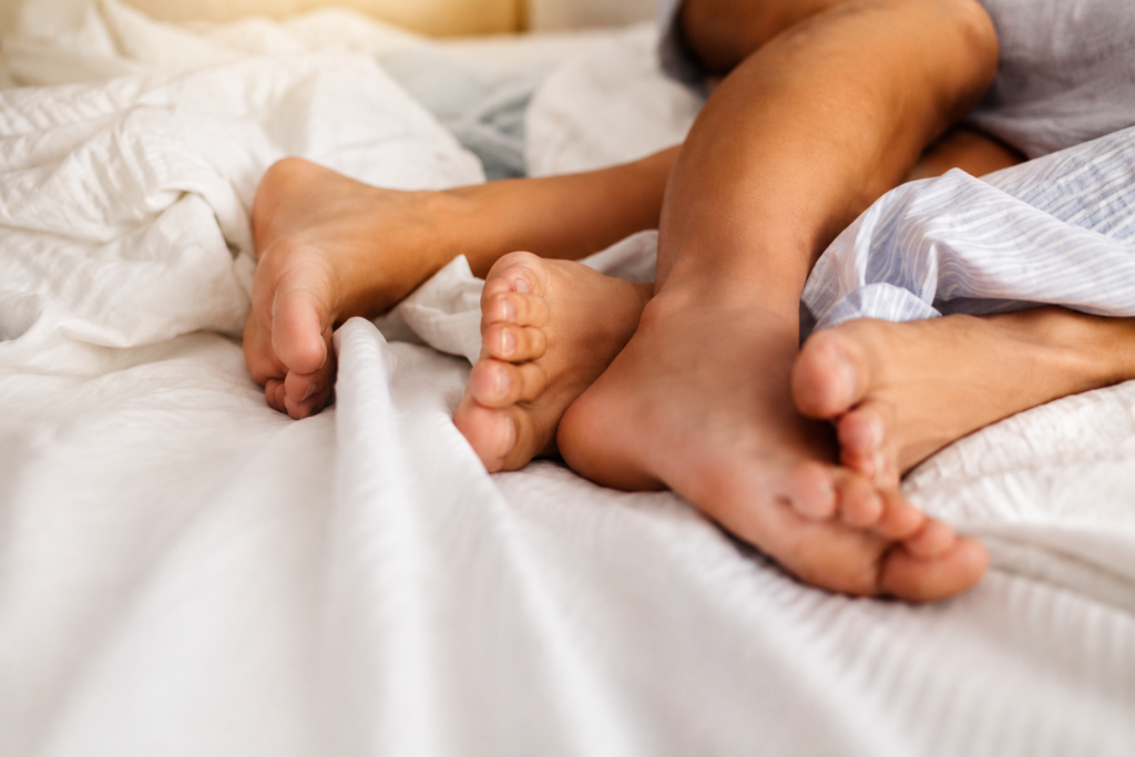 Pieds d’un couple allongé dans un lit, illustrant l’intimité, la fatigue chronique et la baisse de libido liée à l’épuisement du corps.